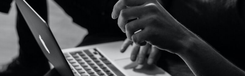 A grayscale image of a person’s hands typing on a laptop keyboard.