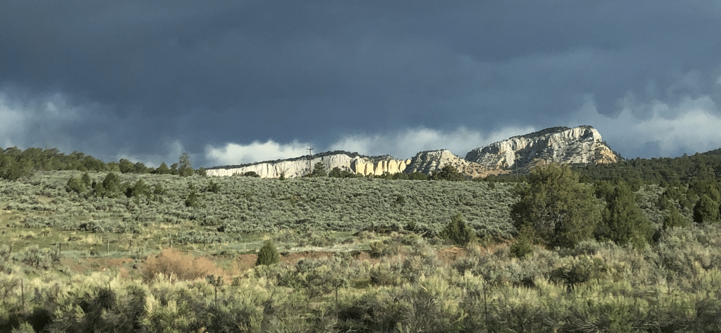 A landscape image featuring rugged mountains in the distance. The sky above the mountains is dark and filled with storm clouds.