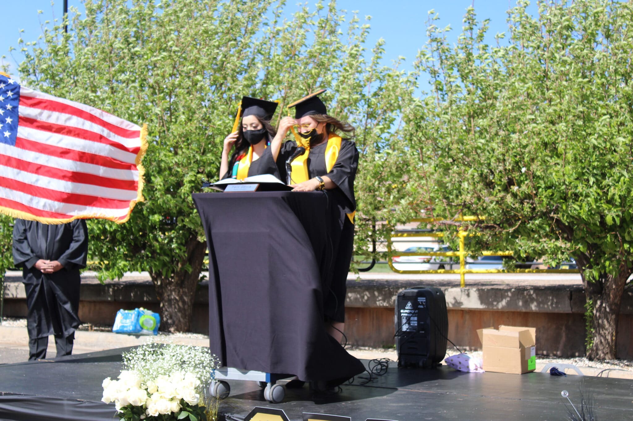 Two students in graduation gowns and caps on stage