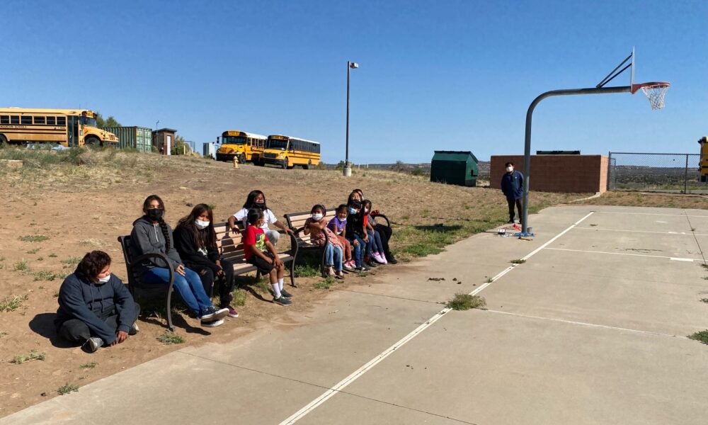 Students seated on a bench in a school courtyard.