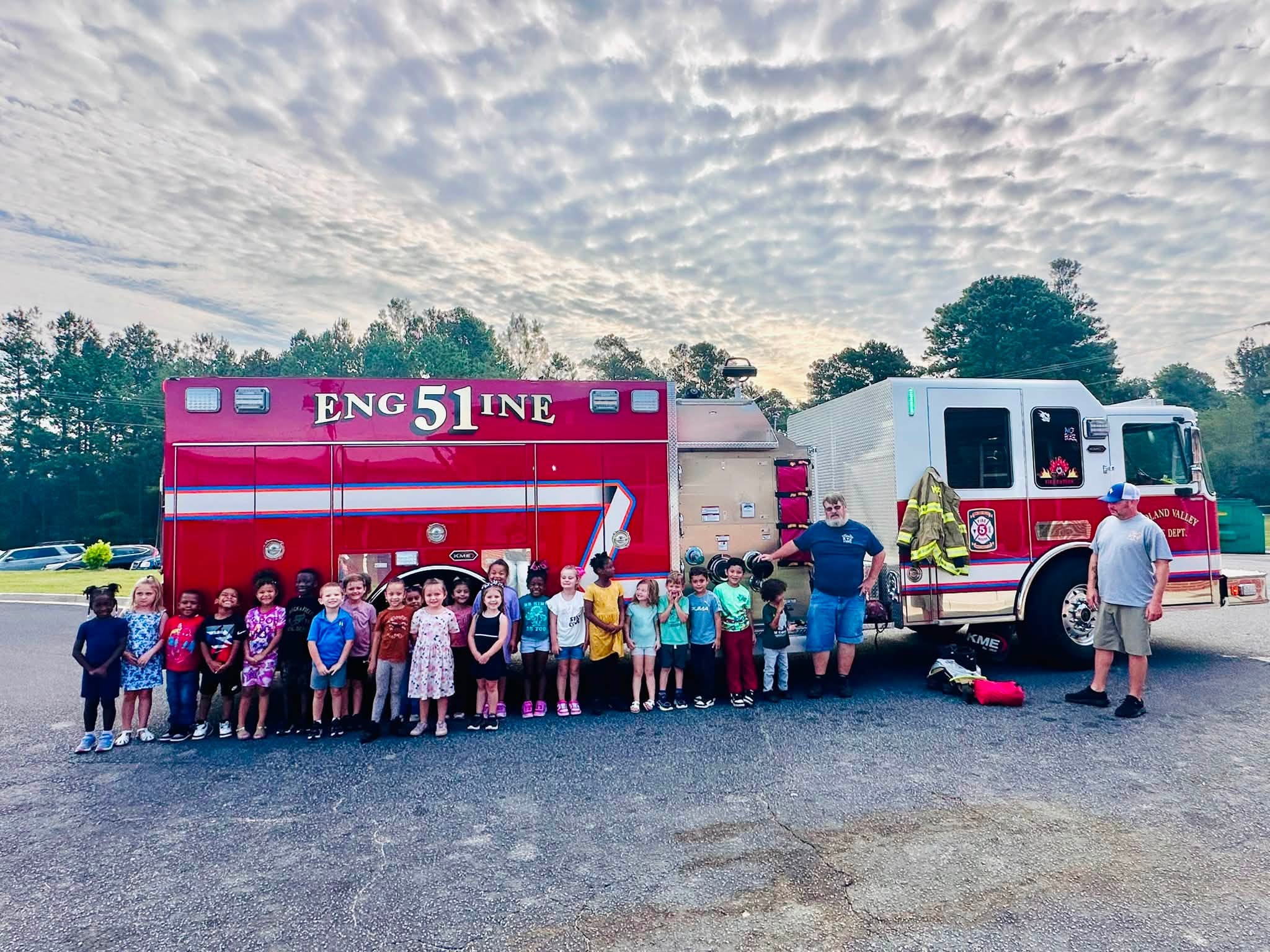 A class of kindergarten students stand in front of a firetruck.
