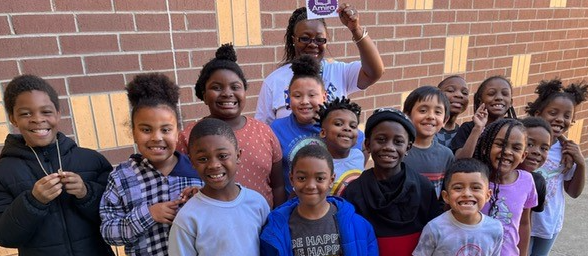 Students standing with their teacher celebrating an Amira award for accomplishing 100% of their lessons completed for the week!