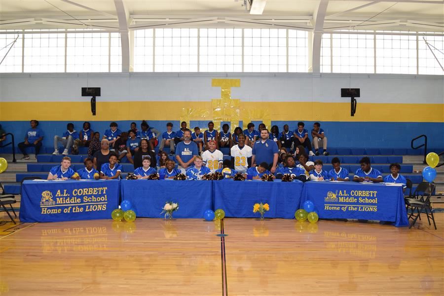 7th grade students signing for football in gymnasium with coaches