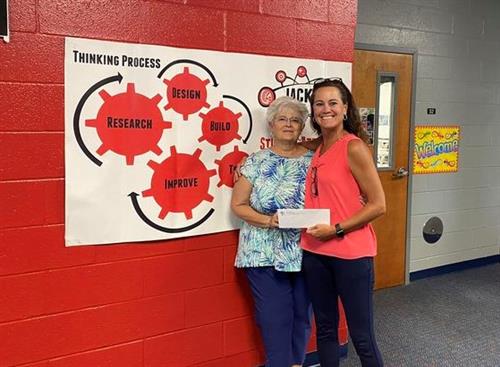 Two women smiling at the camera next to the school's "thinking process"