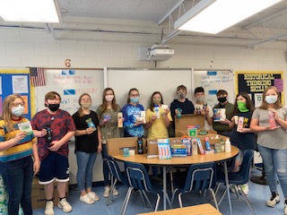 This is a large group of students holding up various items and looking at the camera with covid mask on a