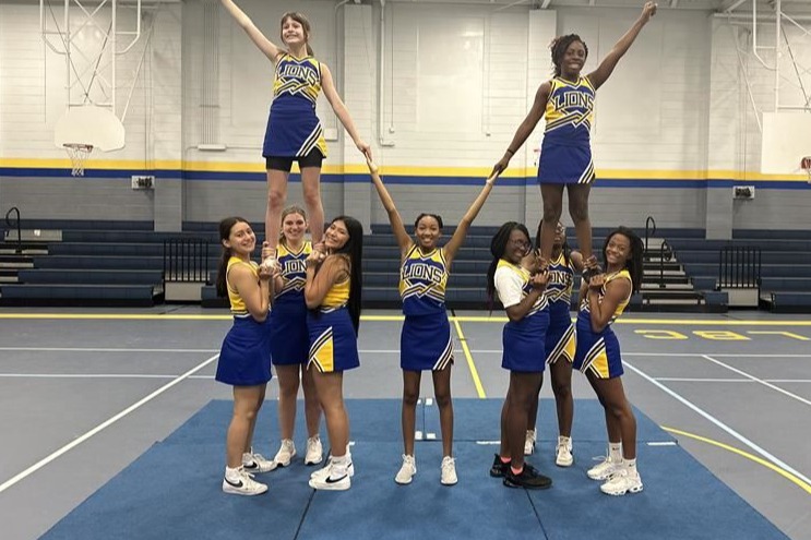 This is a image of a group of girls at cheer  camp. They are doing a stunt beside each other and holding a half high V with their hands...connecting to a cheerleader on the floor 