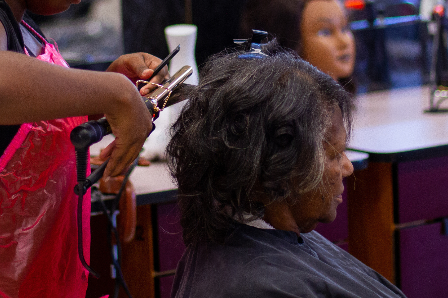 student's hands using curling iron to curl woman's hair