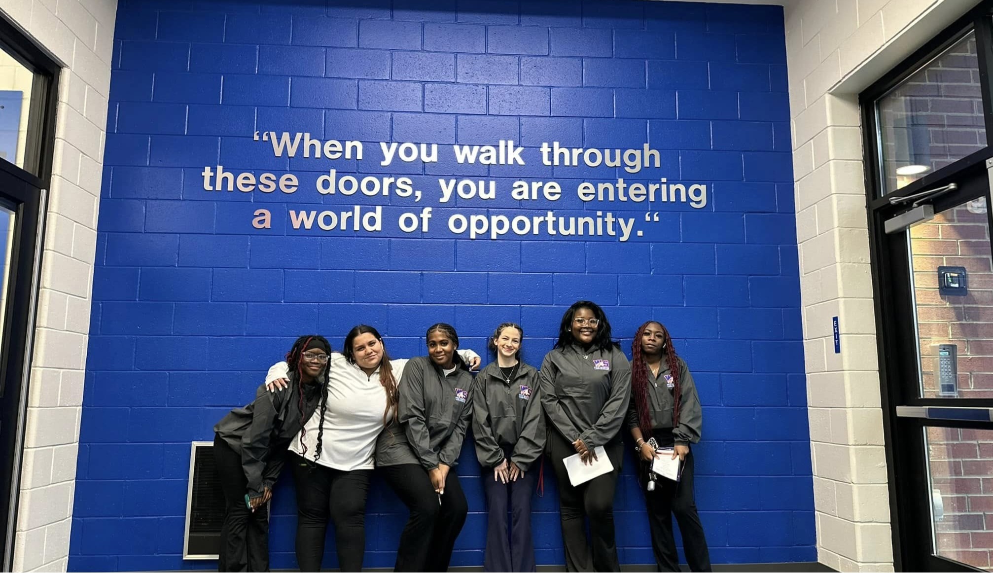 Students pose in the entrance way of the school under an inspirational quote.