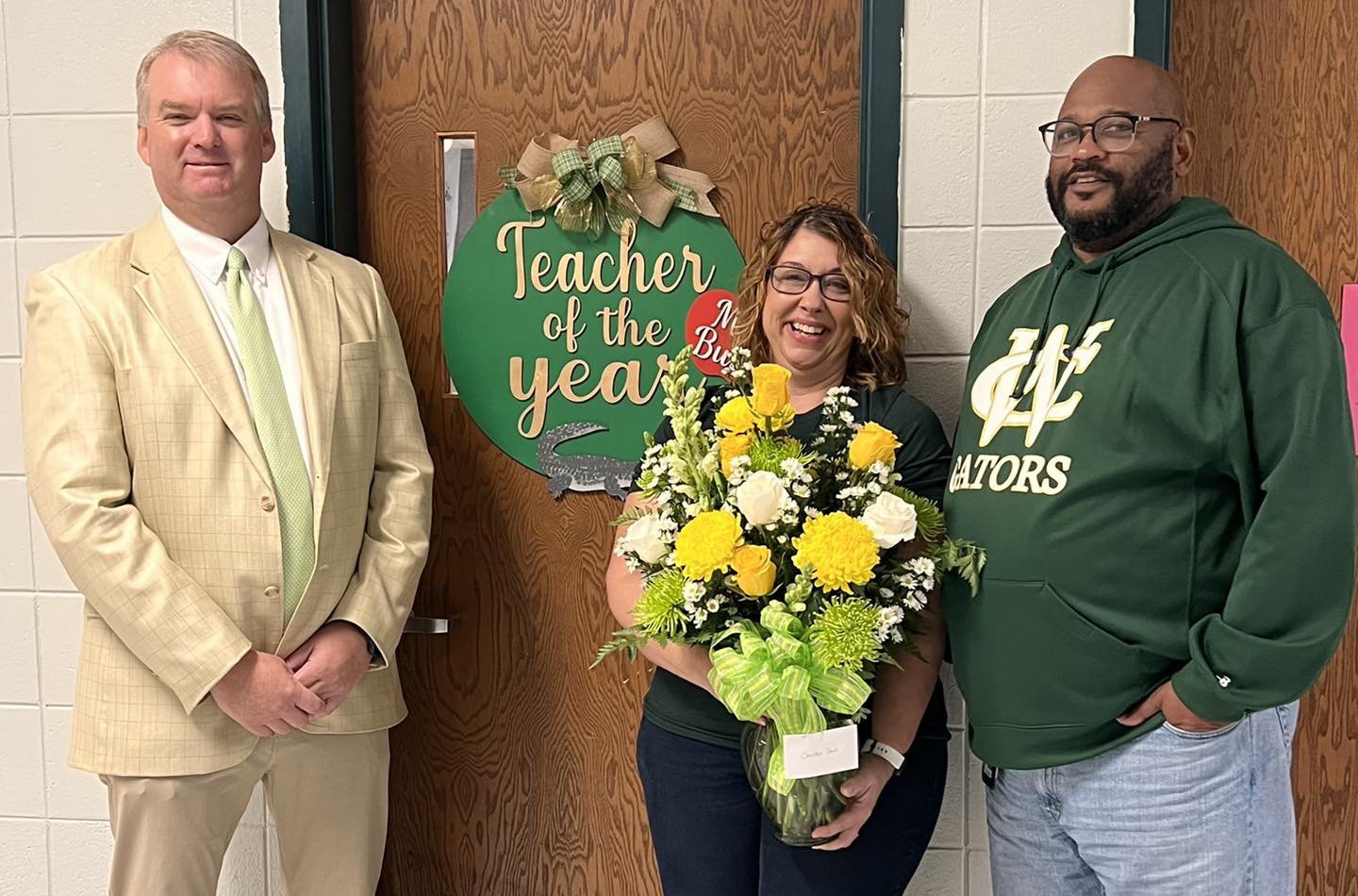 teacher with bouquet of yellow and green flowers in front of "teacher of the year" sign