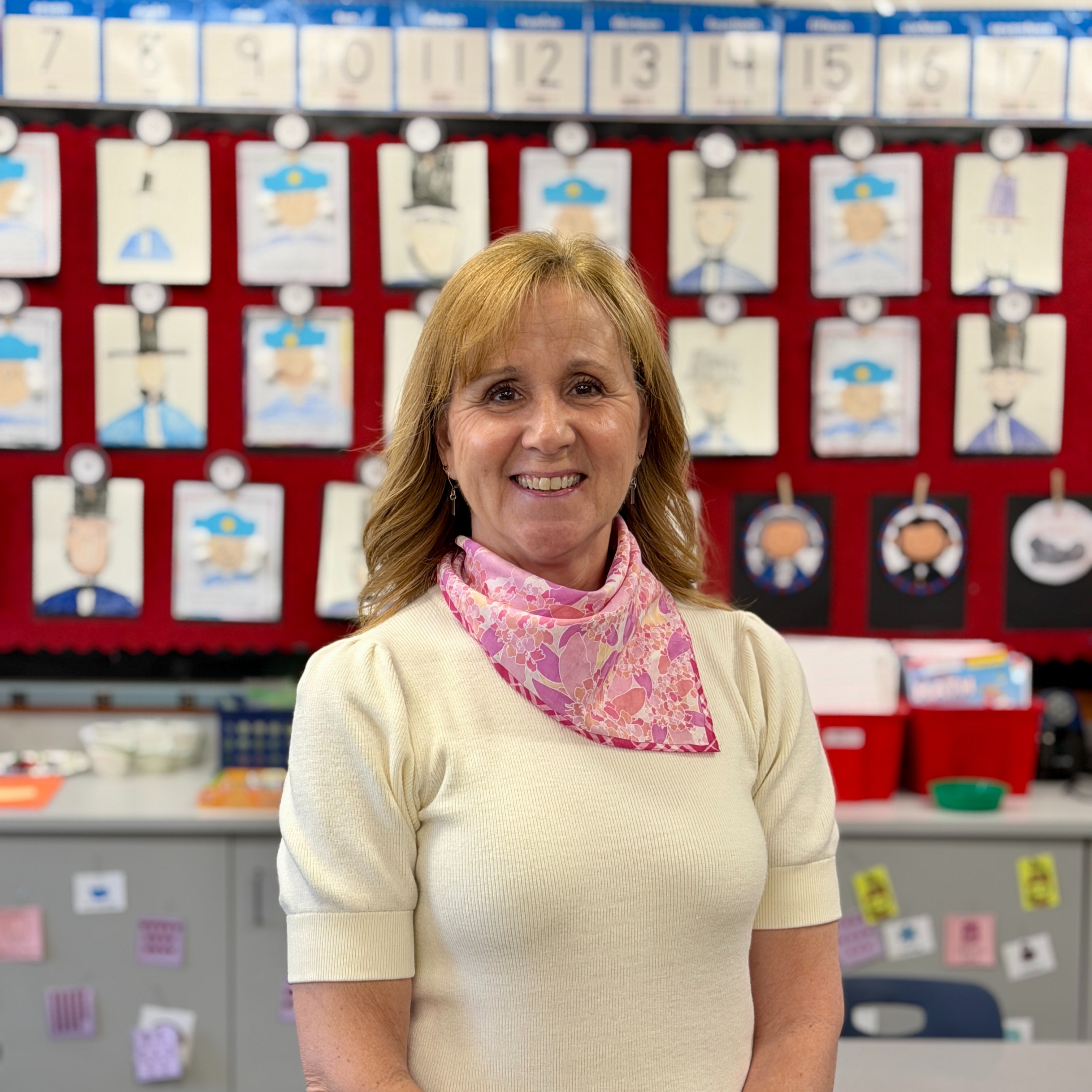 Mrs. Iaccuo's staff headshot in her clasroom with projects behind her.