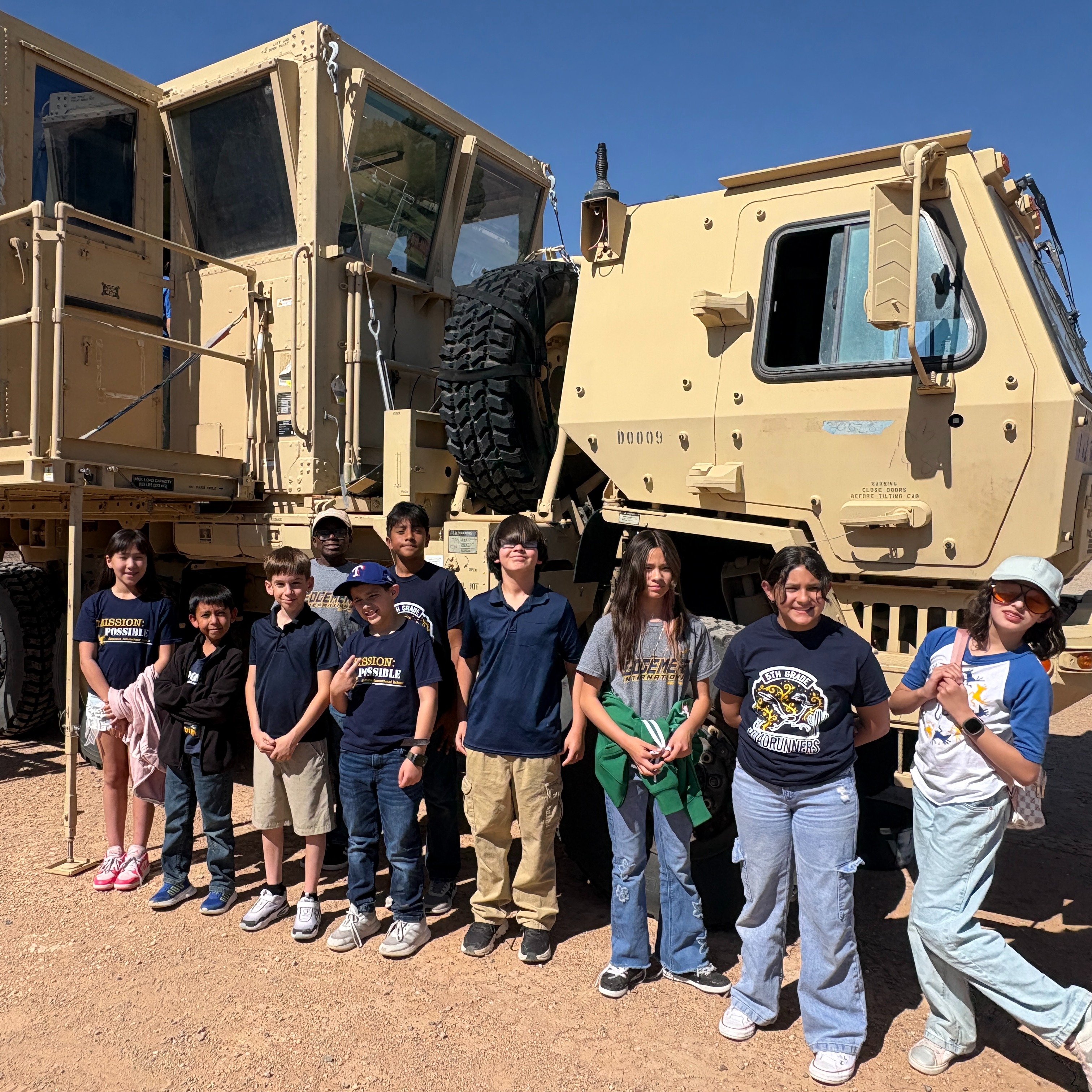 Group of students standing in front of military vehicle