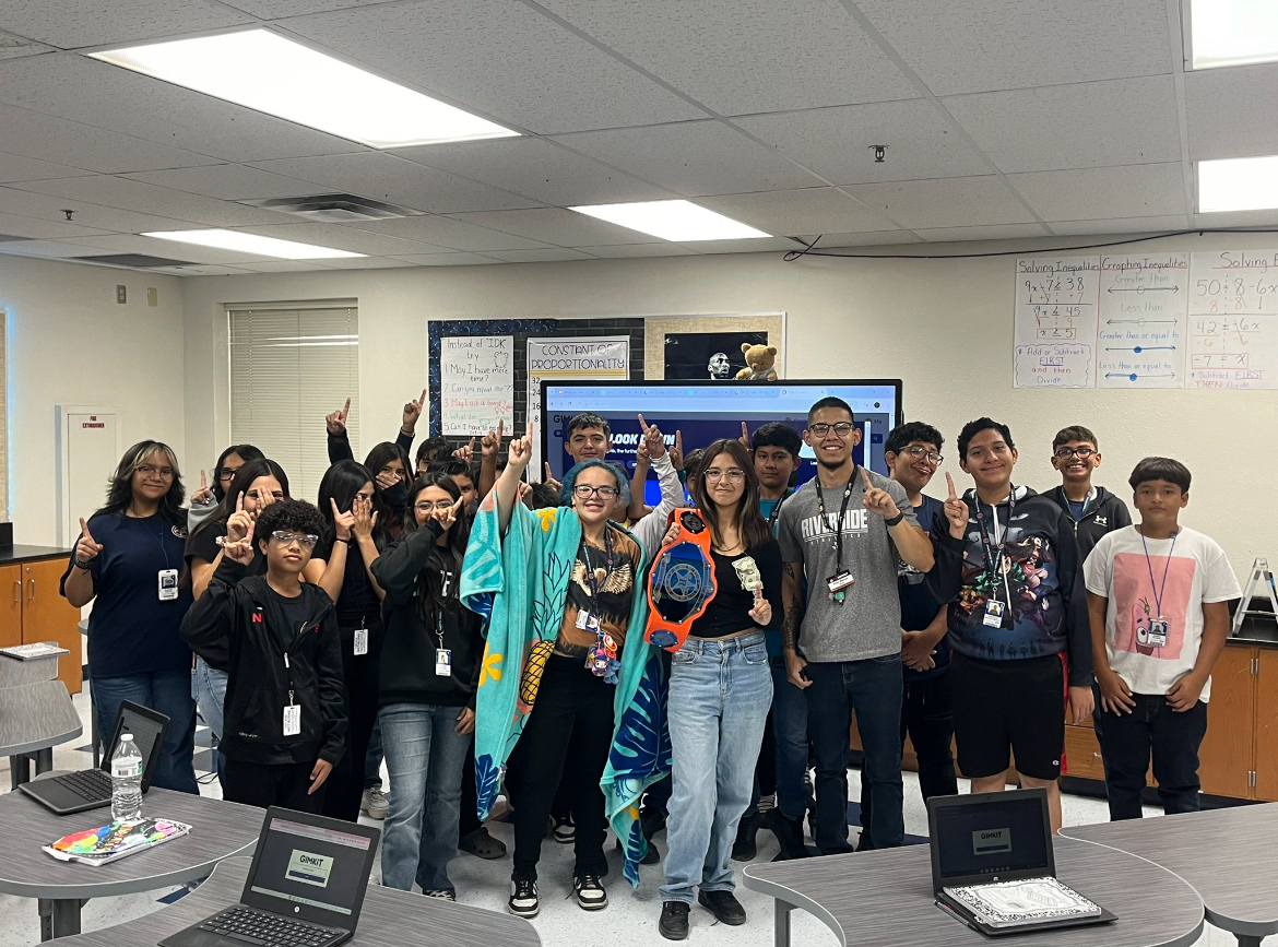 Students in the classroom standing in a group to pose for the picture while holding the championship belt for winning the attendance  challenge with their teacher