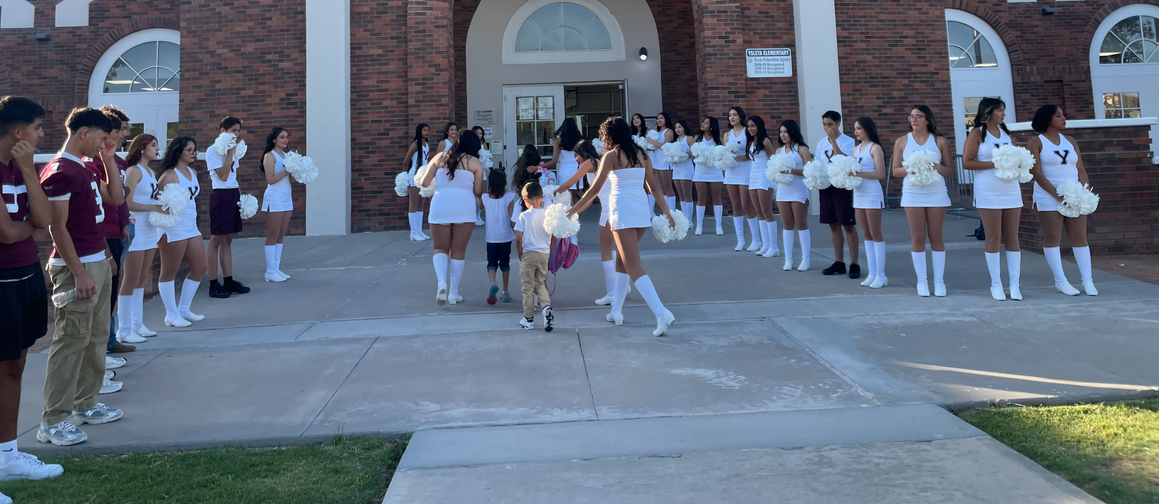 Ysleta High School cheerleaders and football players  welcome Ysleta Elementary students early one morning