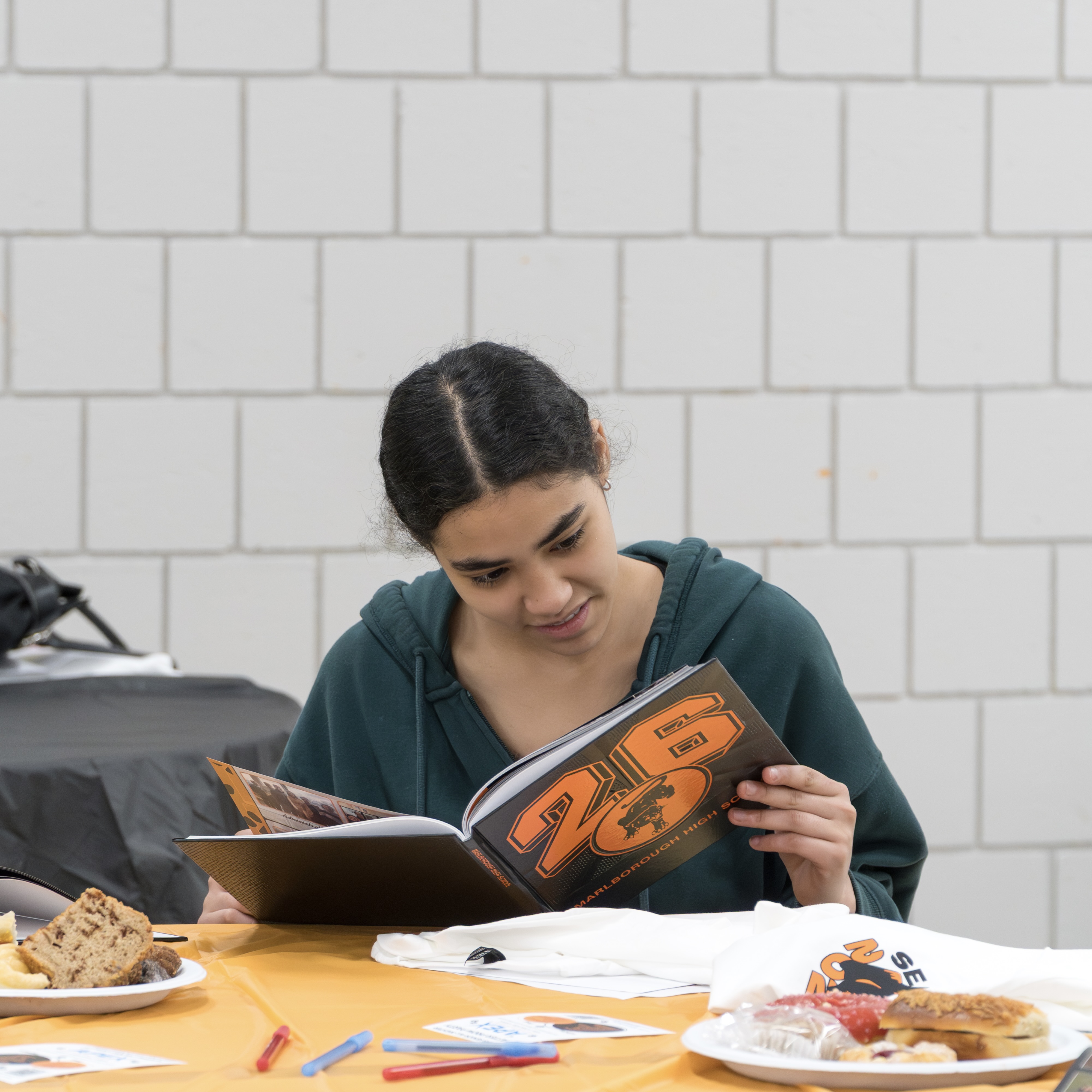 A woman reads a magazine with "25" on the cover, sitting at a table with food.