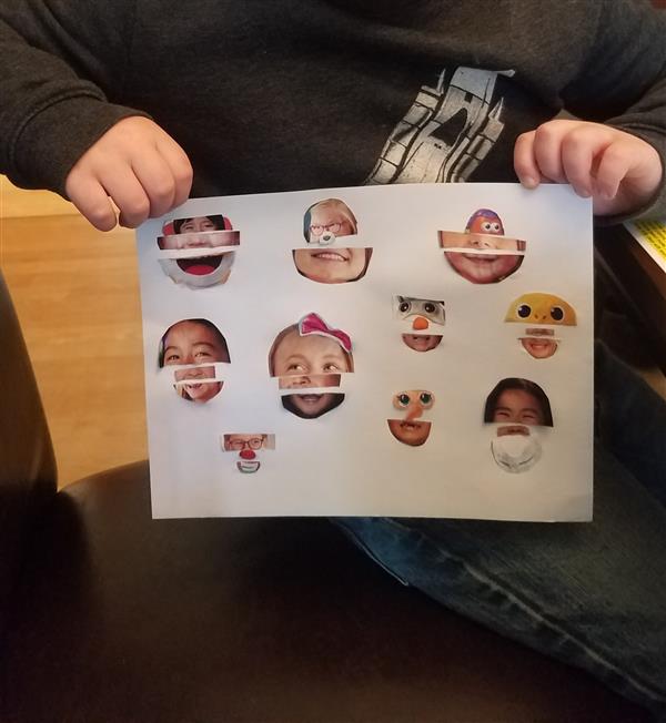 Child displaying paper with various face drawings.