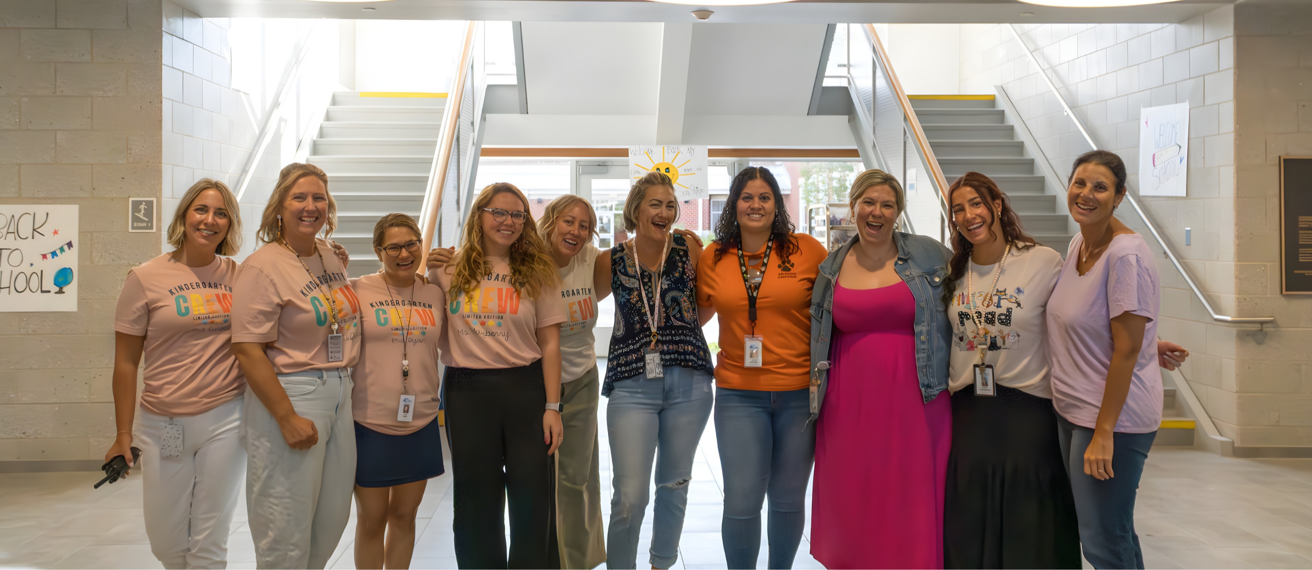 Nine Goodnow female staff members in casual clothing pose for a photo inside a school hallway with stairs.