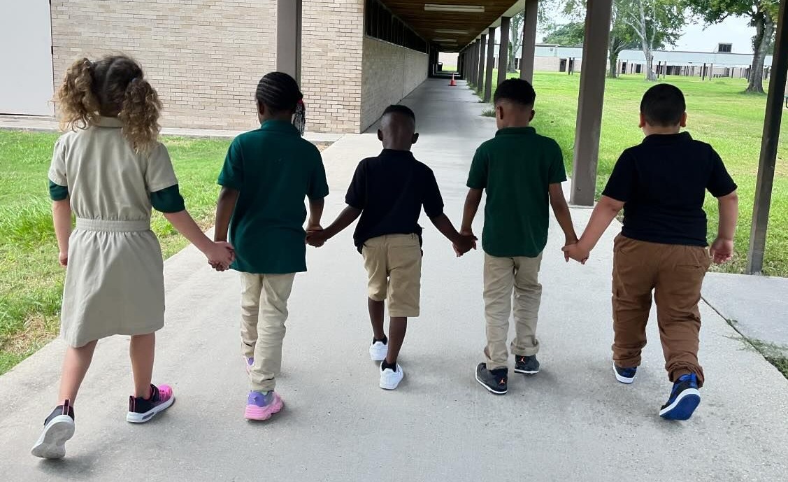 5 students holding hands walking on the sidewalk