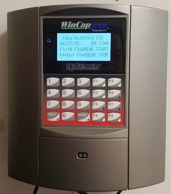 A time clock mounted on a wall. The clock has a digital display that reads "The time clock is ready to start" The keypad has several function keys, including F1-IN, F5-Break Start, F4-Out, and F8-Break Stop. There are also number keys from 0 to 9.