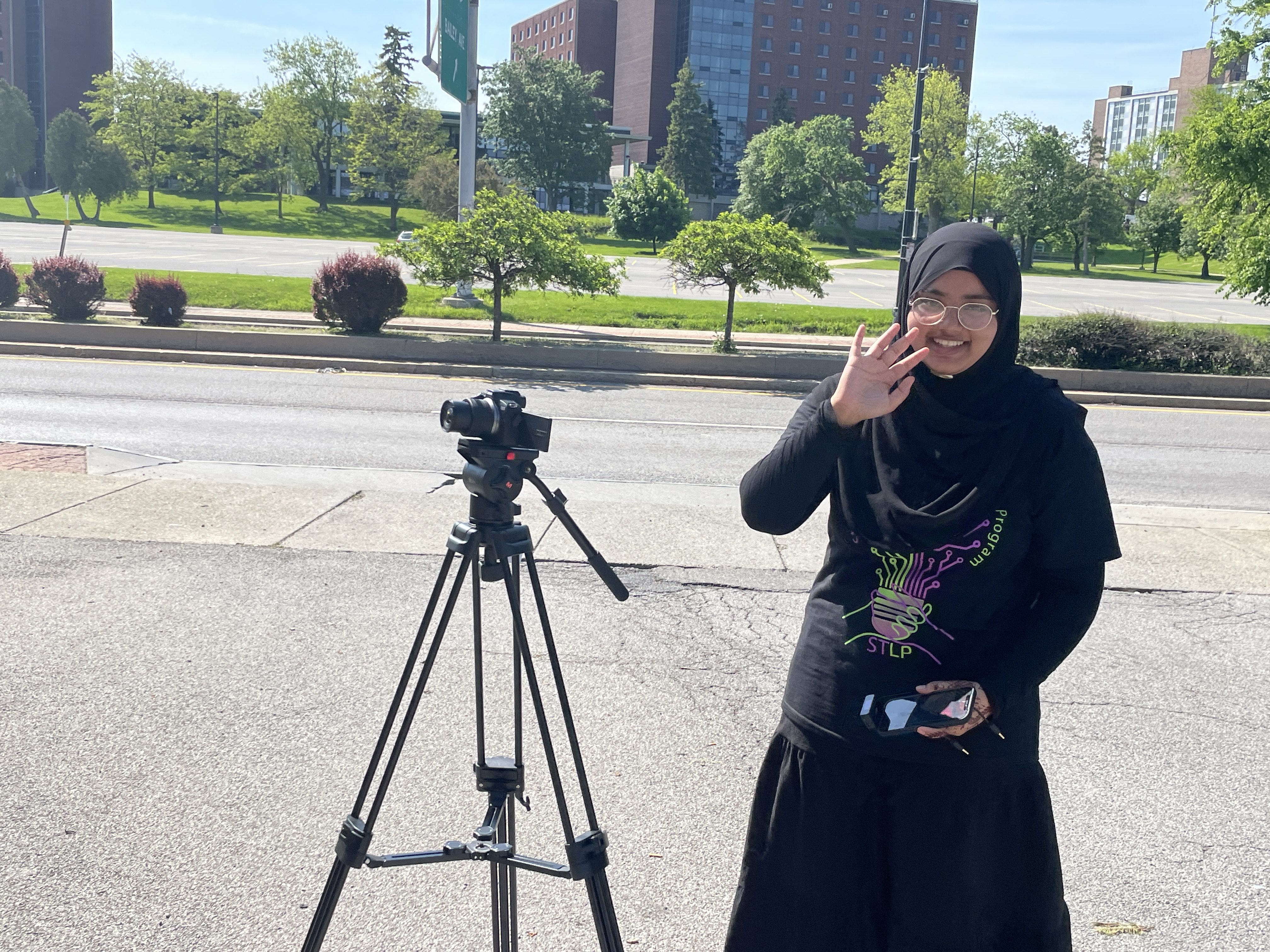 Student waving with a camera