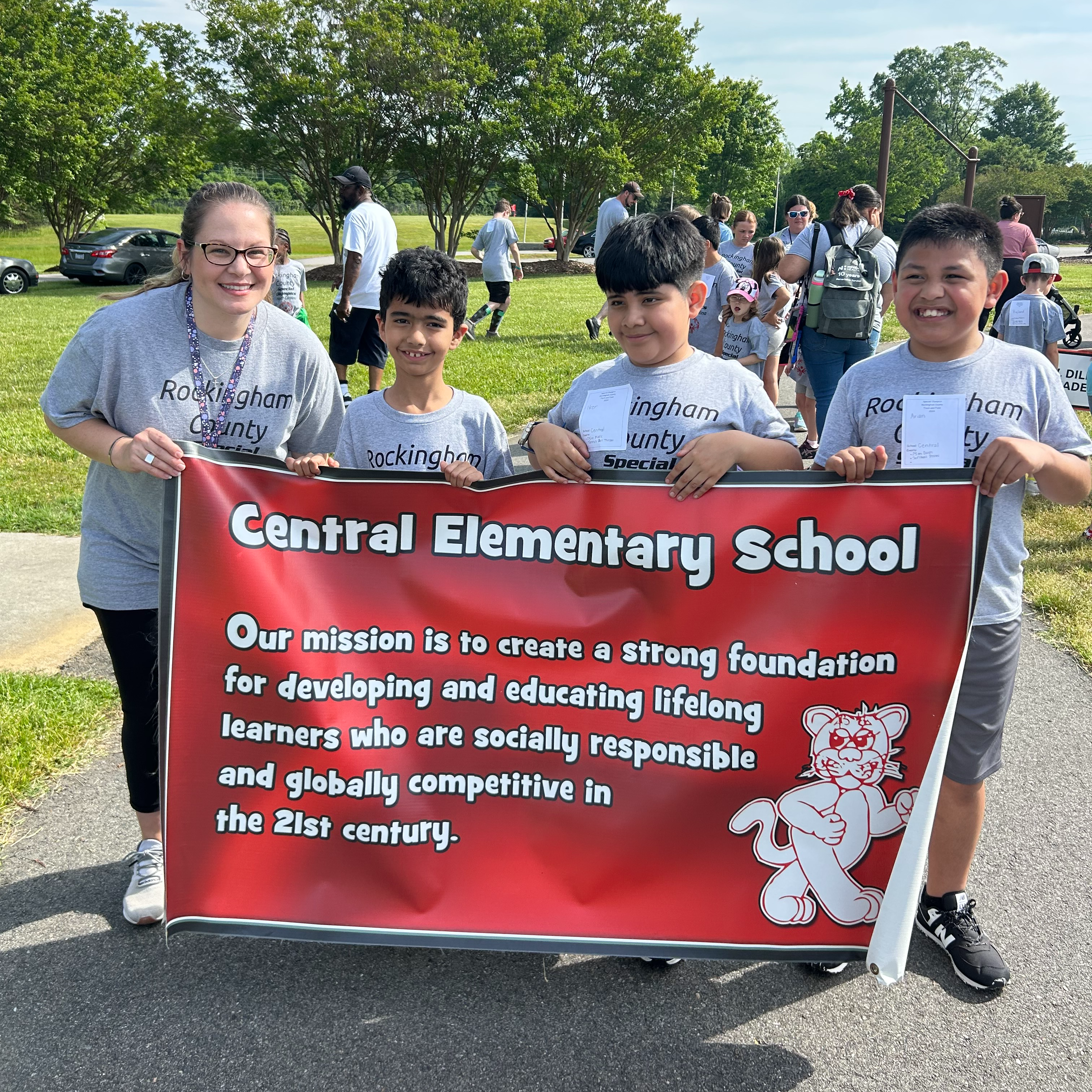 one teacher and three boys holding a Central Elementary School banner