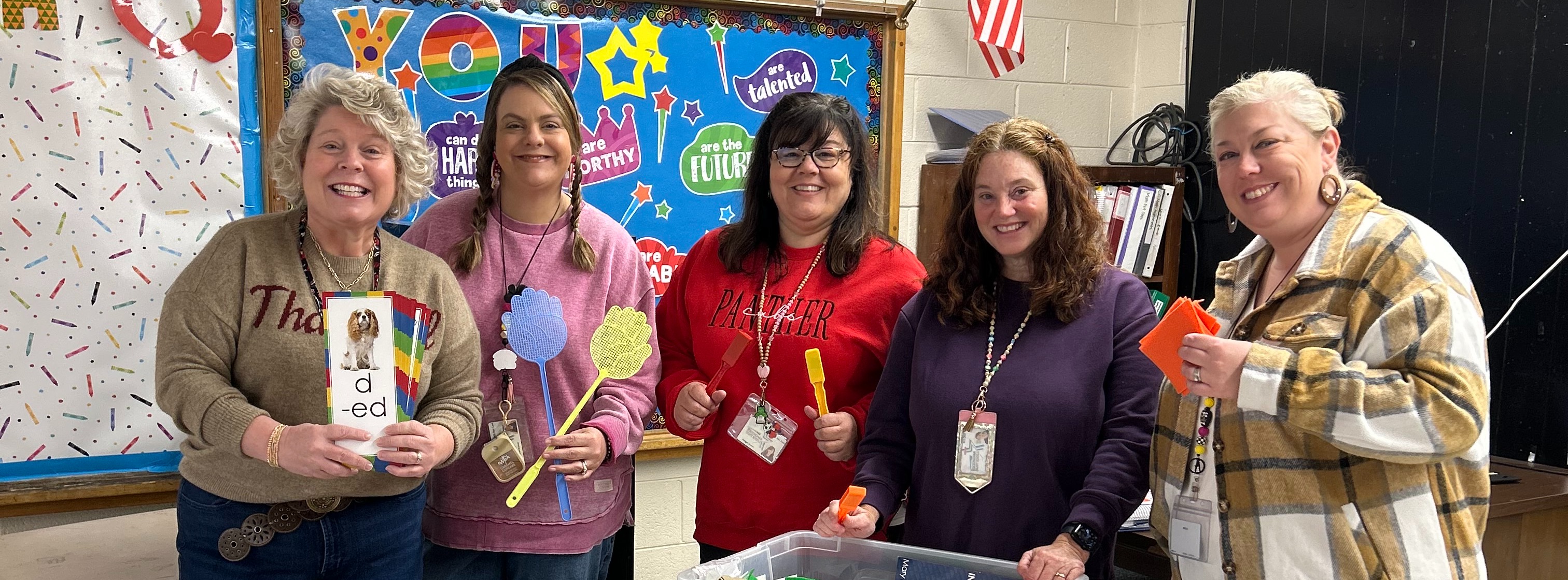 a group of 5 teachers stand together in classroom holding reading kit tools