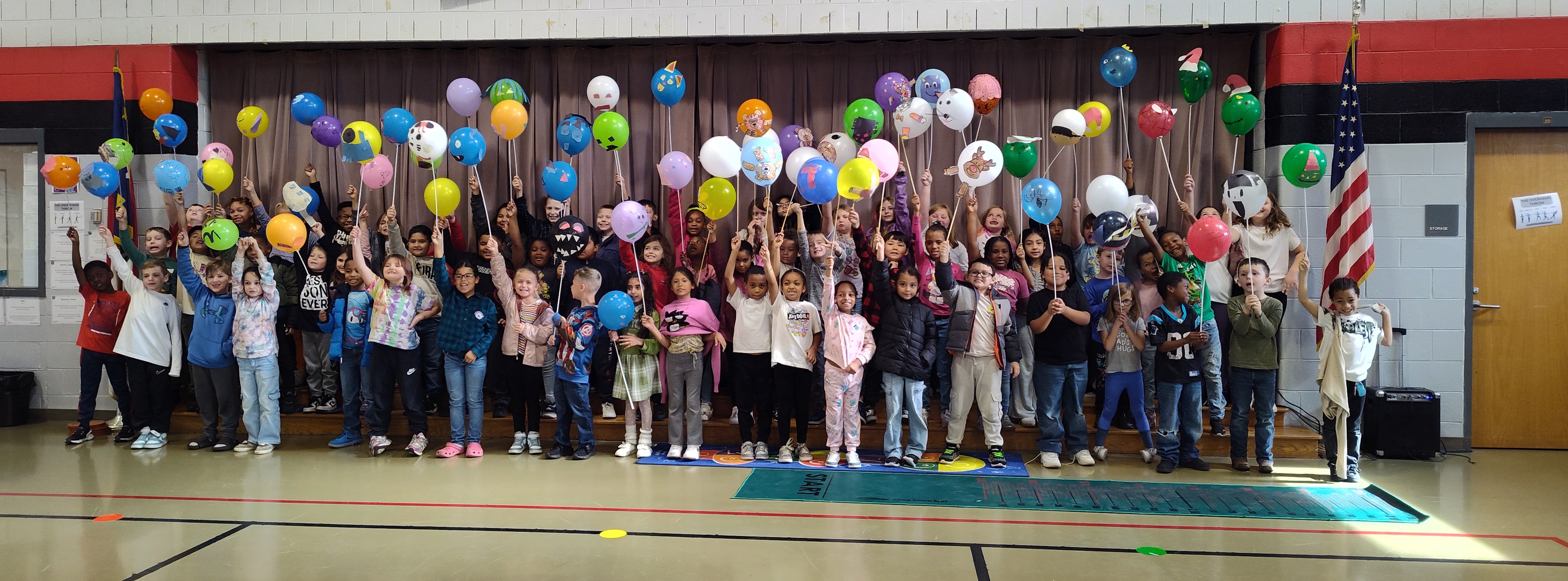 students stand at the front of the gymnasium holding their balloon creations