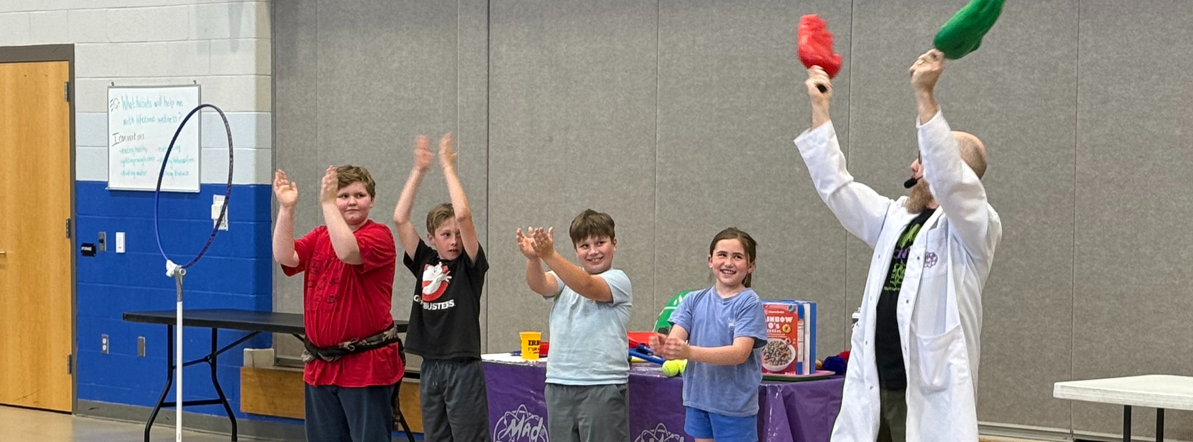 man clapping large red and blue plastic hands with children clapping in background