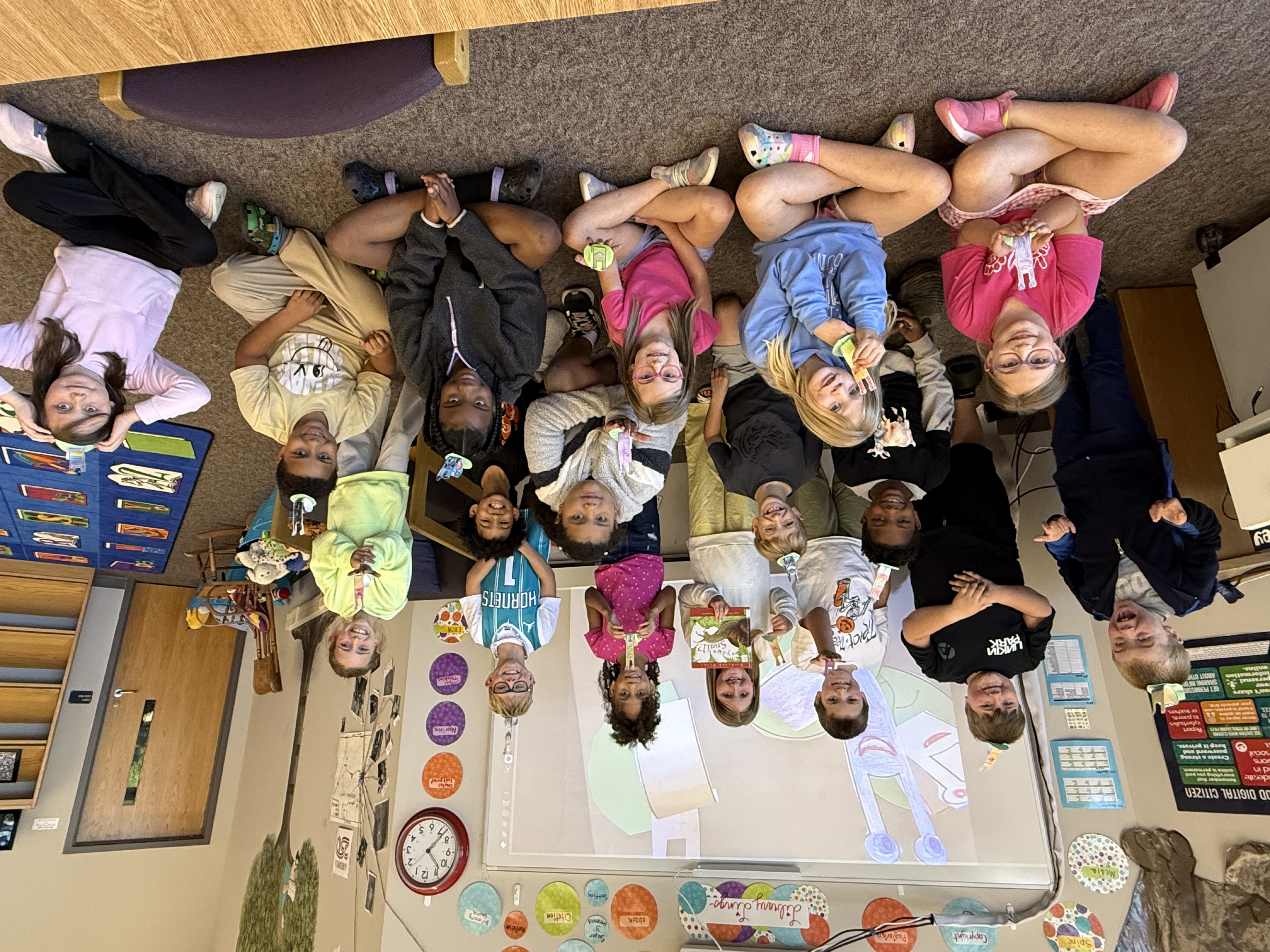 students sitting on floor and standing together holding snail craft