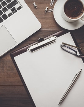 Clipboard, laptop, cup of coffee, pen and glasses