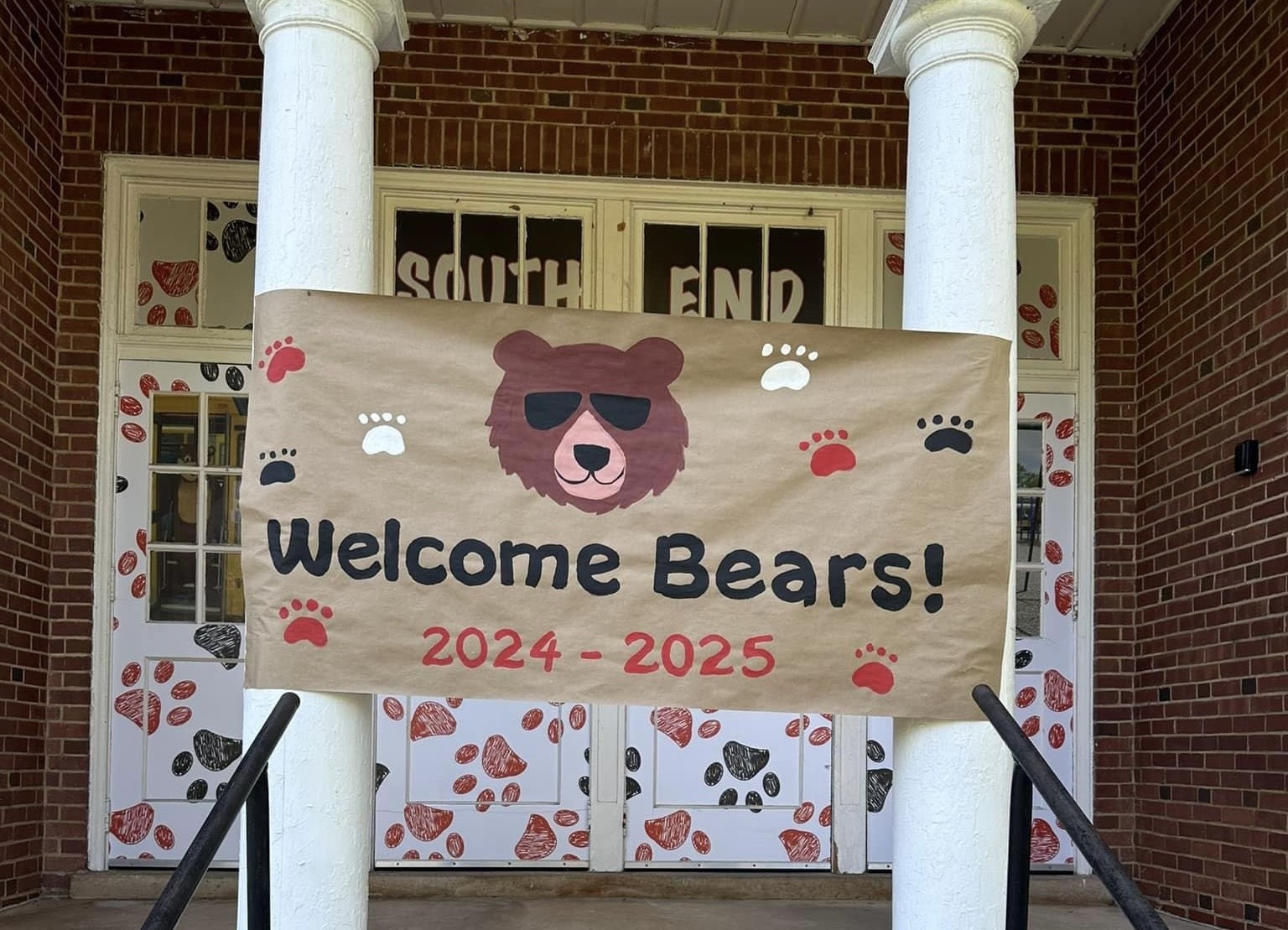 A brown banner across the front of the school building that says. "Welcome Bears 20024-2025." There is the head of a brown bear wearing sunglasses and paw prints in black, red and white..