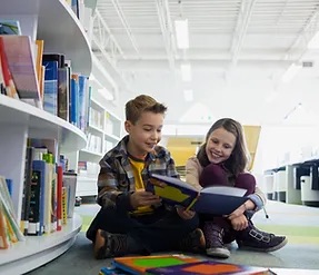 2 young students at a library reading together