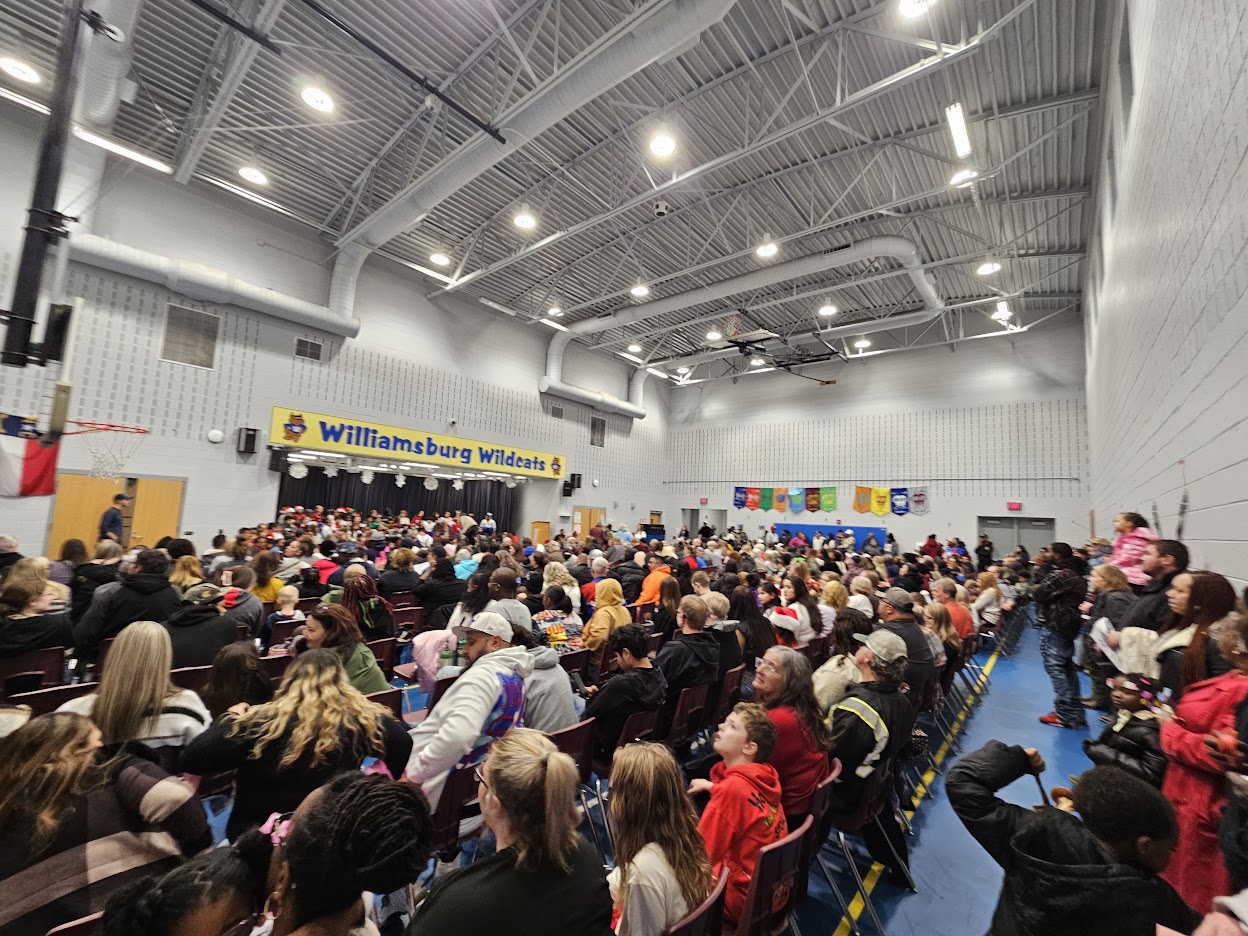 The image shows famiiles seated in the school gym listening to students perform a winter music program during a Title 1 Parent night event.