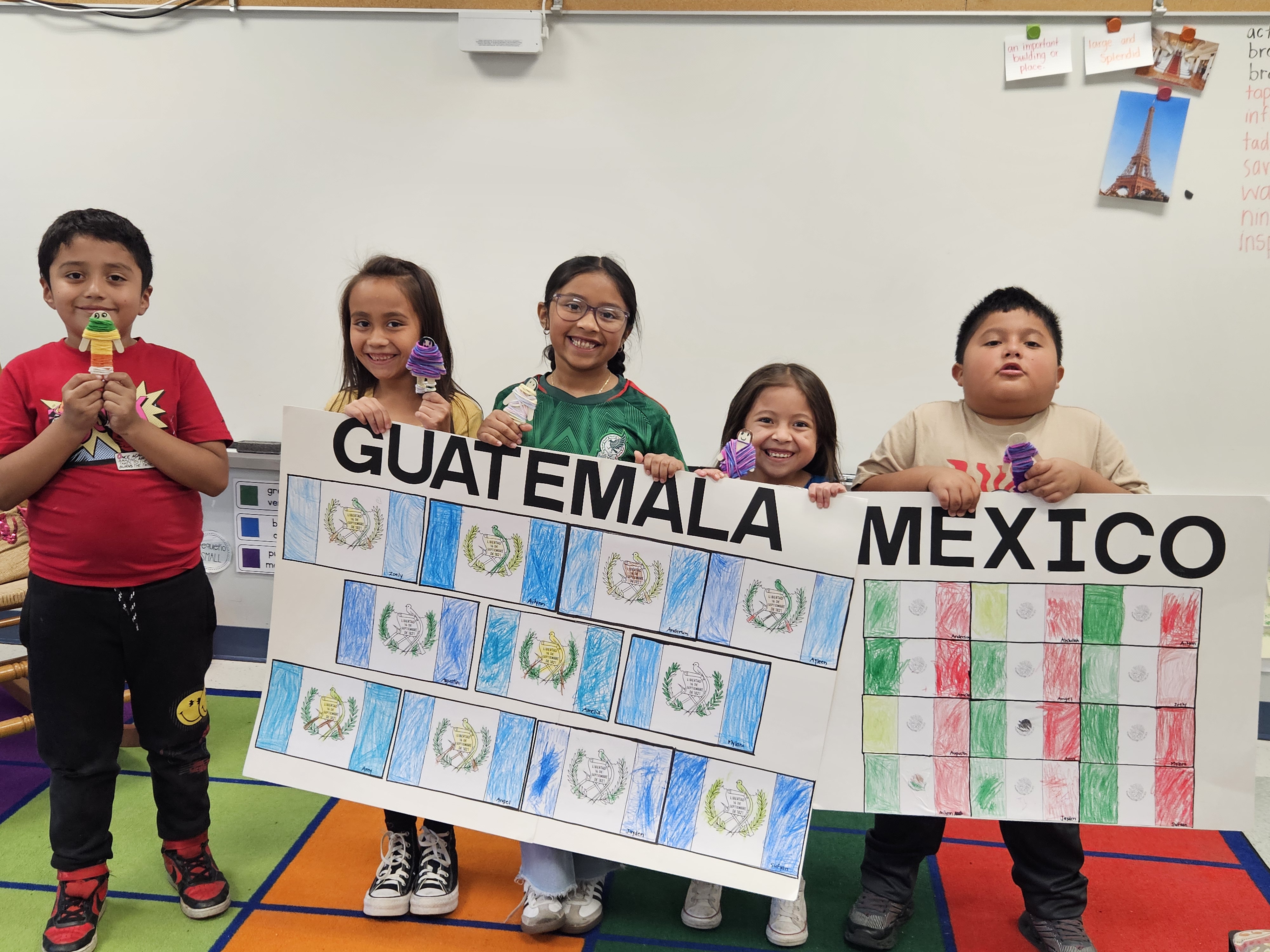 A group of elementary students showing posters they created with flags for Guatemala and Mexico as part of a Hispanic Heritage program