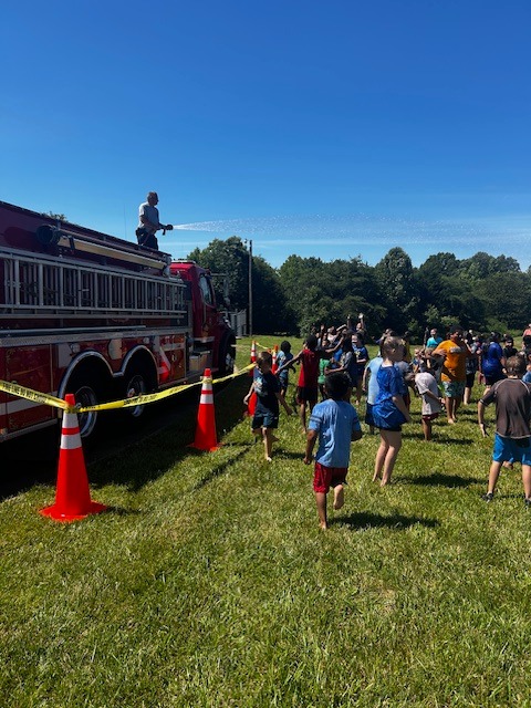Students enjoy being sprayed with water by a fire truck at the end of Field Day