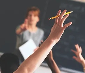 student raising his hand, while the teacher is about to choose him for the answer