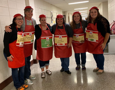 group of teachers, each wearing aprons, each with a banner of a different herb or spice