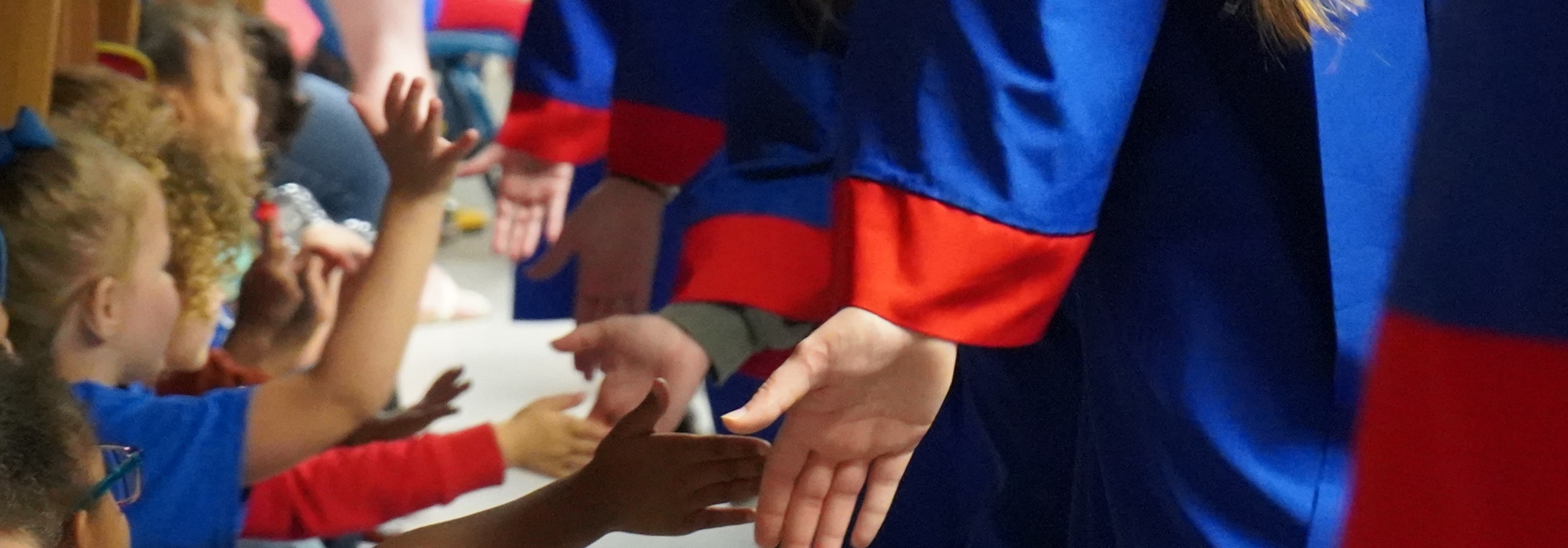 Young children reaching out for high-fives from seniors in blue and red graduation caps and gowns