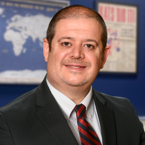 face of white male brown hair black suit red tie with office background