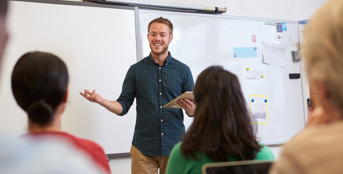 Adult male substitute teacher smiling facing students in front of white board