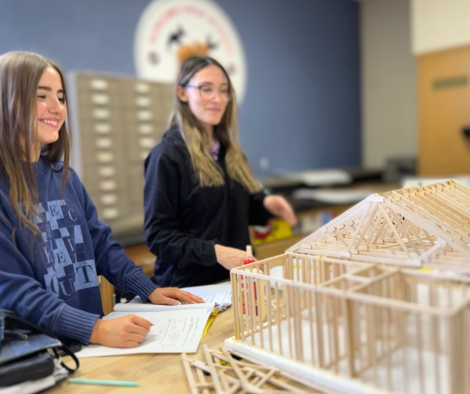 Female students smiling building a structure