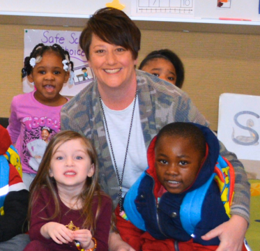 Female teacher smiling with group of elementary students happy in classroom