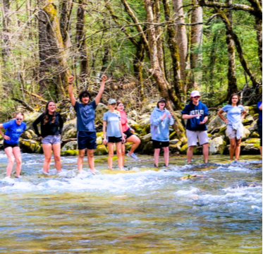 Kids standing in freshwater stream learning about nature with trees in background