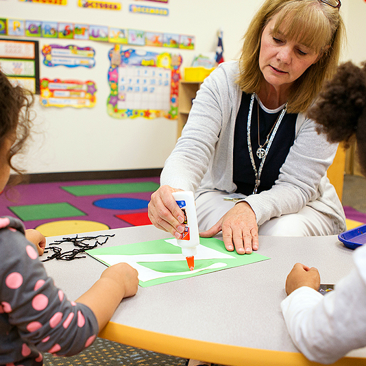 teacher helping students glue paper together