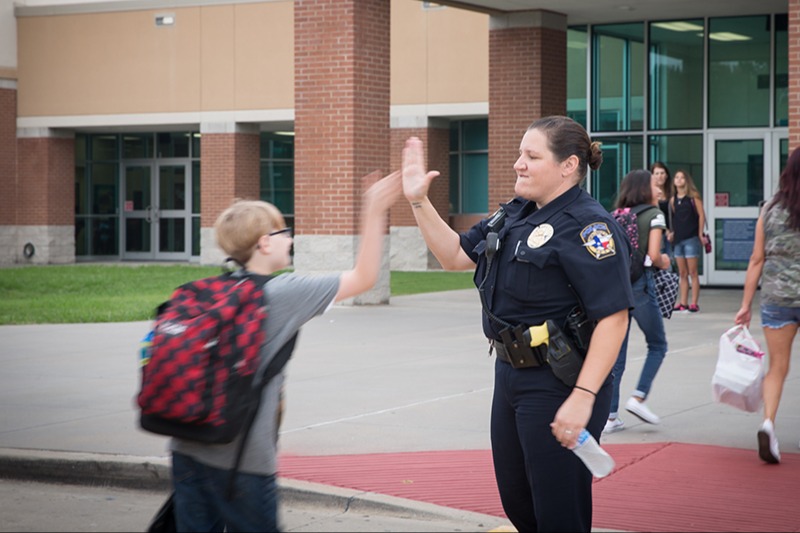 officer high fiving student as he walks  up to school