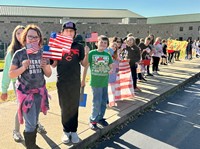 People standing in a line, holding American flags and protest signs.