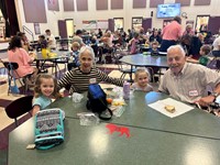 This is a heartwarming photo of an elderly couple and their grandchildren enjoying a meal together at what appears to be a cafeteria.