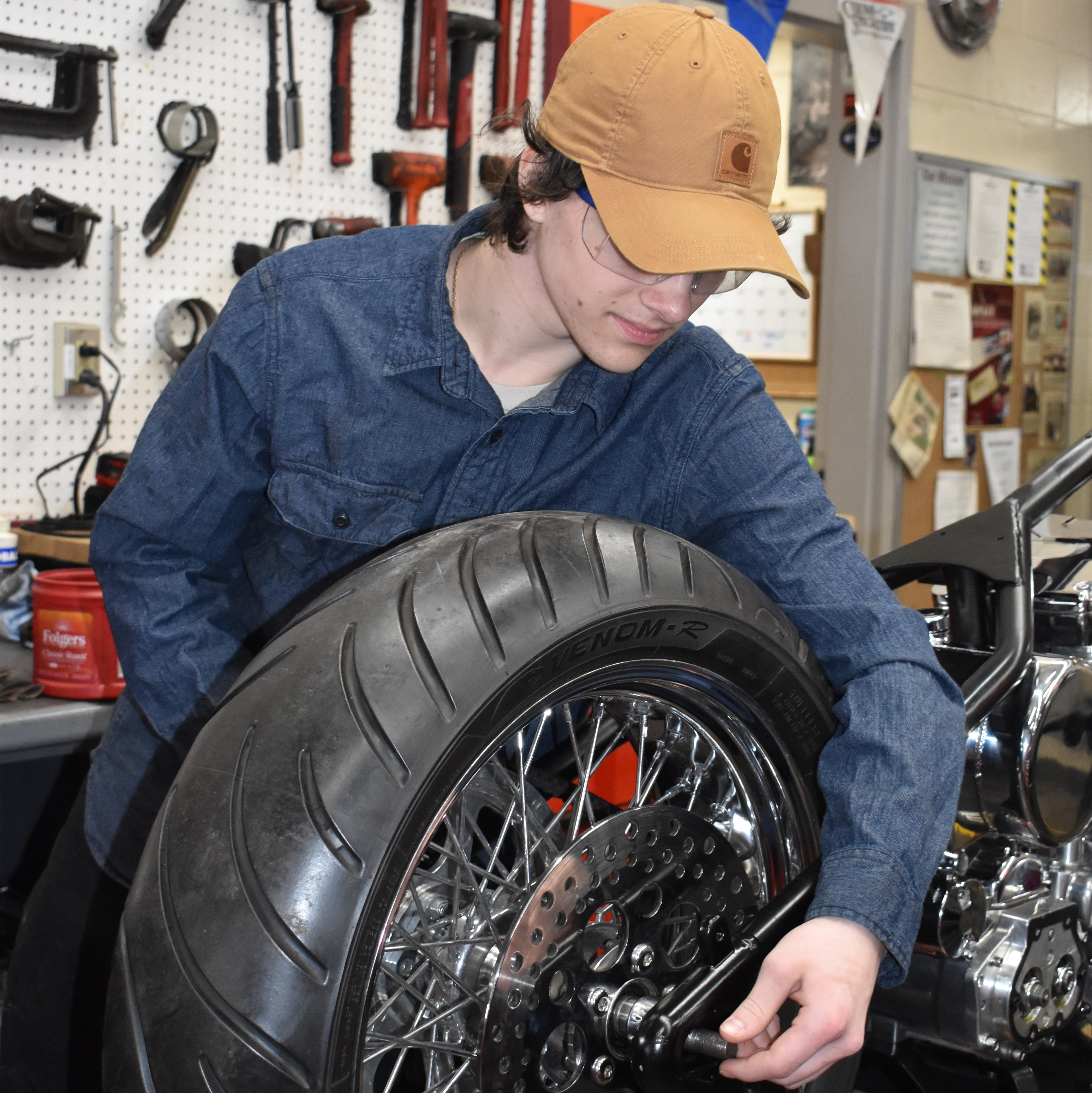 A person working on the underside of a lifted vehicle in a garage, surrounded by tools.