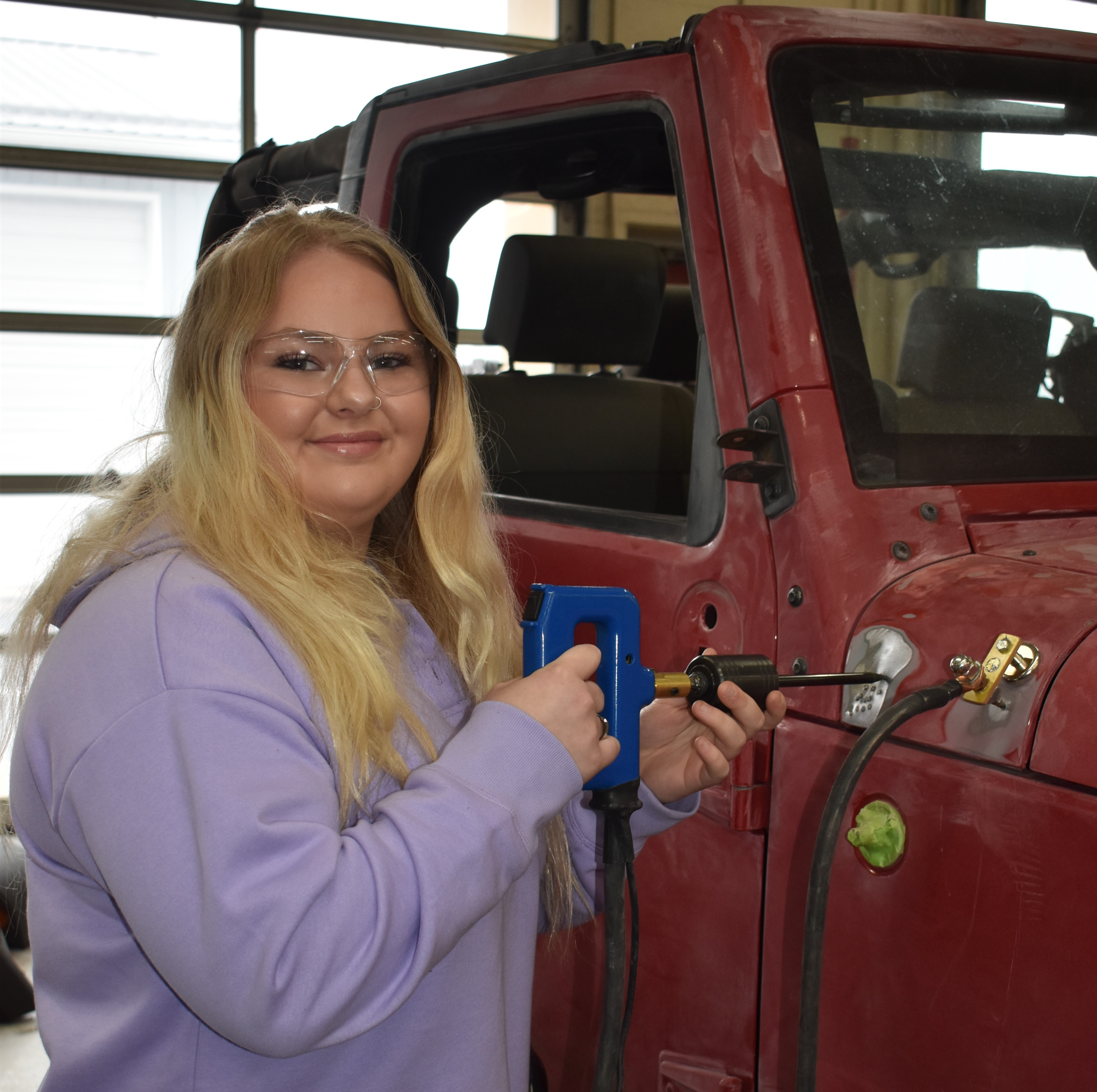 A person working on the underside of a lifted vehicle in a garage, surrounded by tools