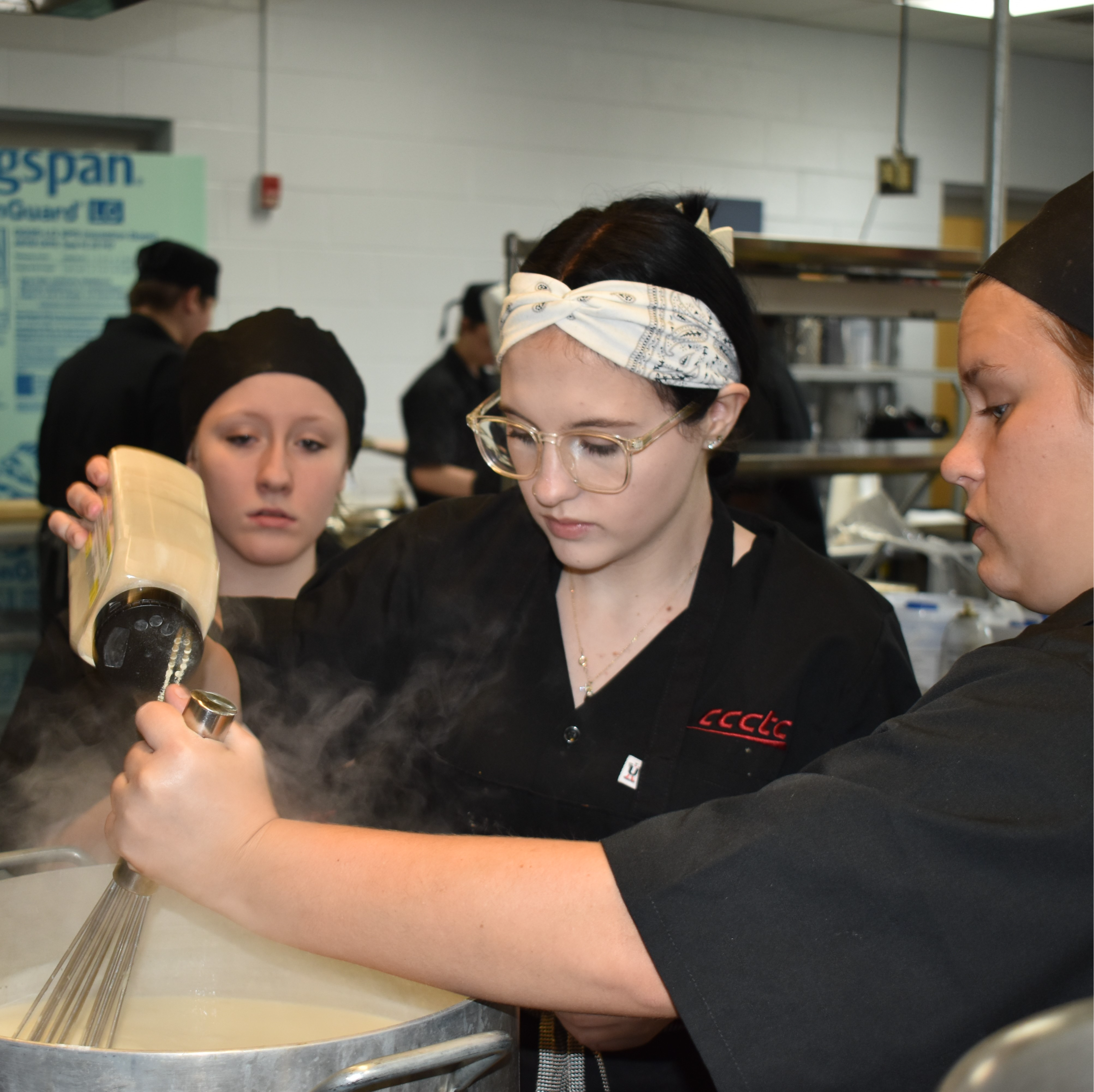 Professional chefs in black attire busily cooking on stovetops in a commercial kitchen