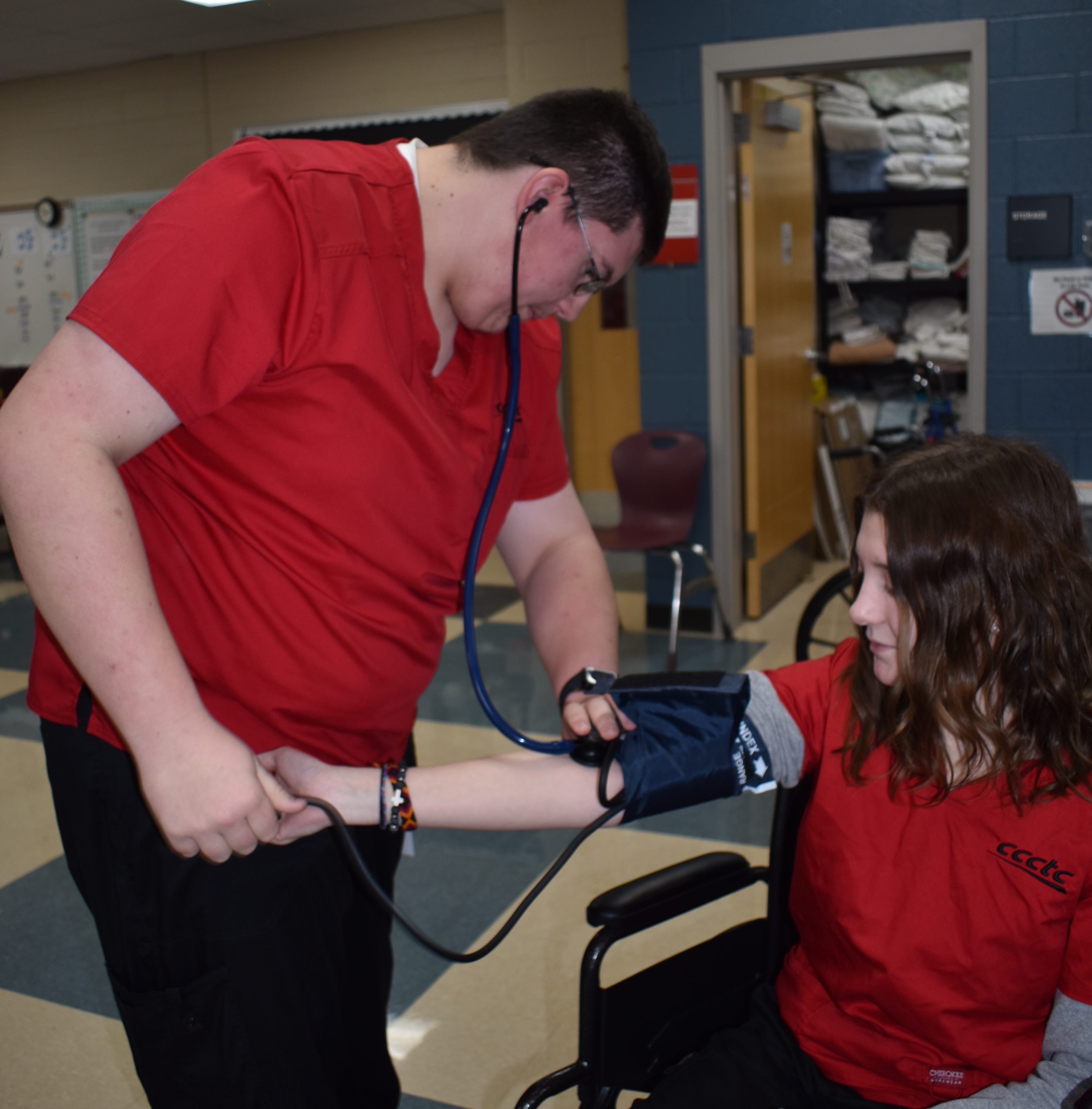 Two individuals clad in red tops are diligently practicing CPR on training manikins within a clinical setting